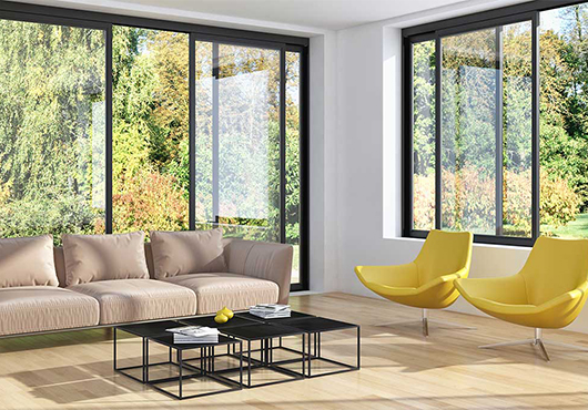 Salon en coin lumineux avec fenêtres et coulissants en aluminium noirs offrant une vue sur la végétation