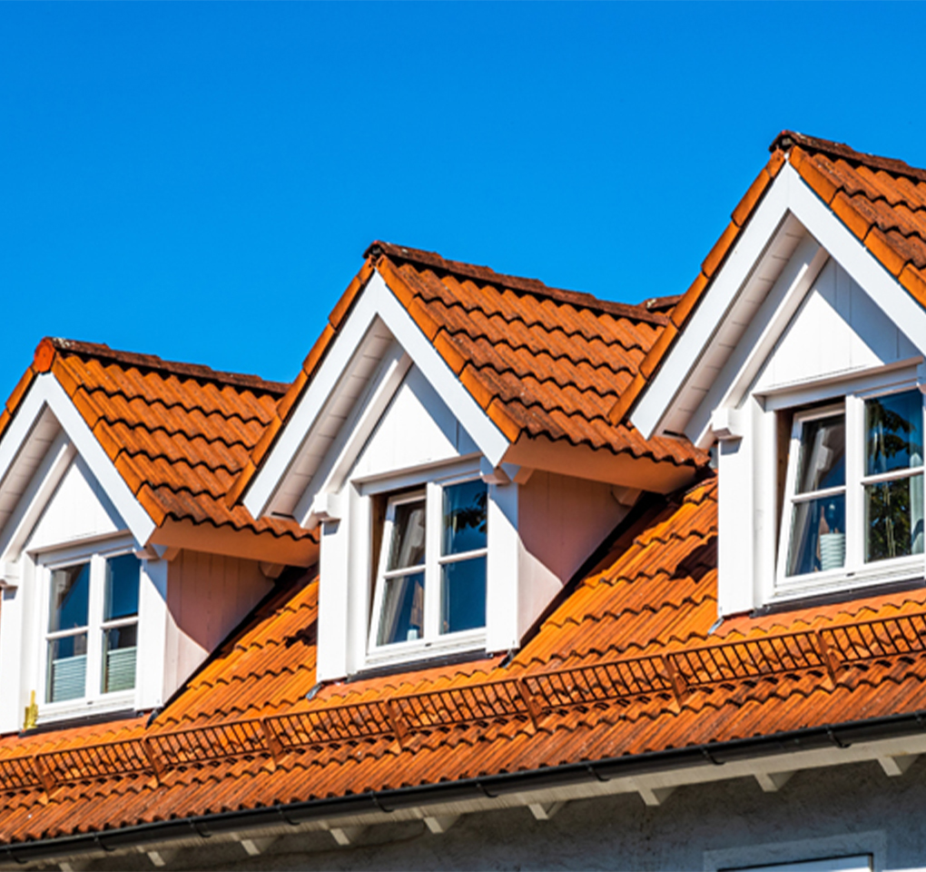 Gros plan sur trois fenêtres de type chien-assis intégrées dans une toiture. Ces ouvertures verticales émergent du toit incliné apportant du relief et du caractère à la façade.