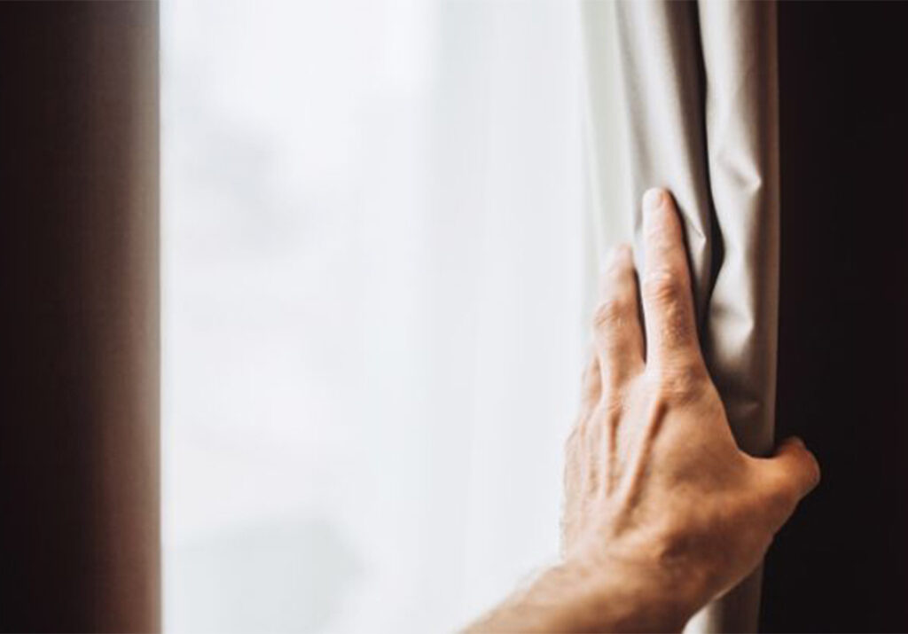 Épais rideau thermique gris tiré devant une fenêtre par une main, créant une barrière contre le froid extérieur et renforçant l’isolation thermique de la maison.