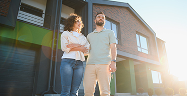 Couple d'une trentaine d'année à l'extérieur devant un immeuble de copropriété avec des fenêtres aluminium neuves