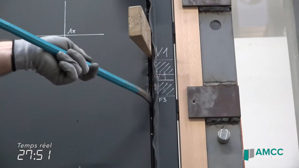 Image extraite de la vidéo du crash test porte réalisé sur une porte prestige AMCC pour tester résistance à l'effraction selon la classe Rc2 et RC3, un homme simule un cambrioleur tentant de fracturer une porte avec un pied de biche
