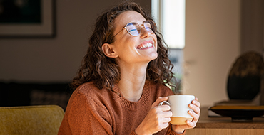 Femme souriante profitant de la luminosité de sont intérieur en buvant un thé dans son canapé