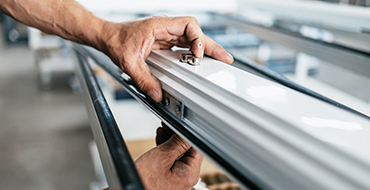 Zoom sur les mains d'un homme travaillant dans une usine AMCC et installant la serrure d'une porte-fenêtre pvc blanche