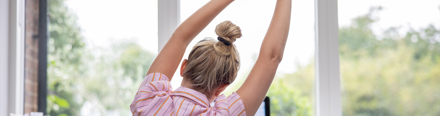 Jeune femme qui s'étire devant une fenêtre en réfléchissant à son projet fenêtres pour faire des économies