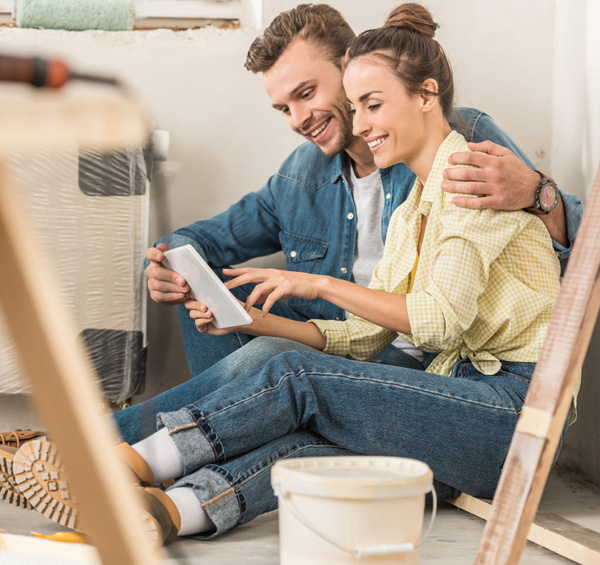 Photo d'un couple installé chez eux par terre un peu au milieu de travaux de peinture décoration en train de configurer leur porte d'entrée sur le configurateur AMCC