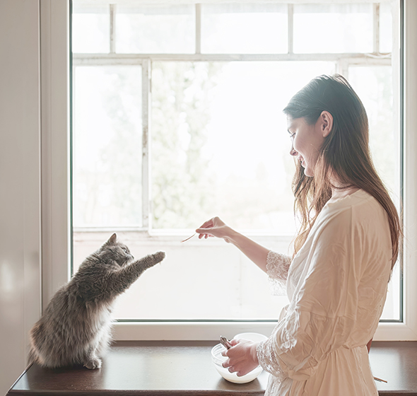 Femme donnant a manger à son chat devant une fenêtre blanche en PVC