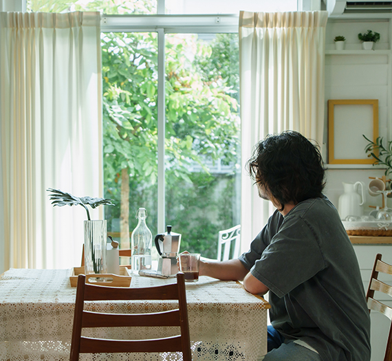 Homme qui boit son café devant sa baie vitrée face à son jardin